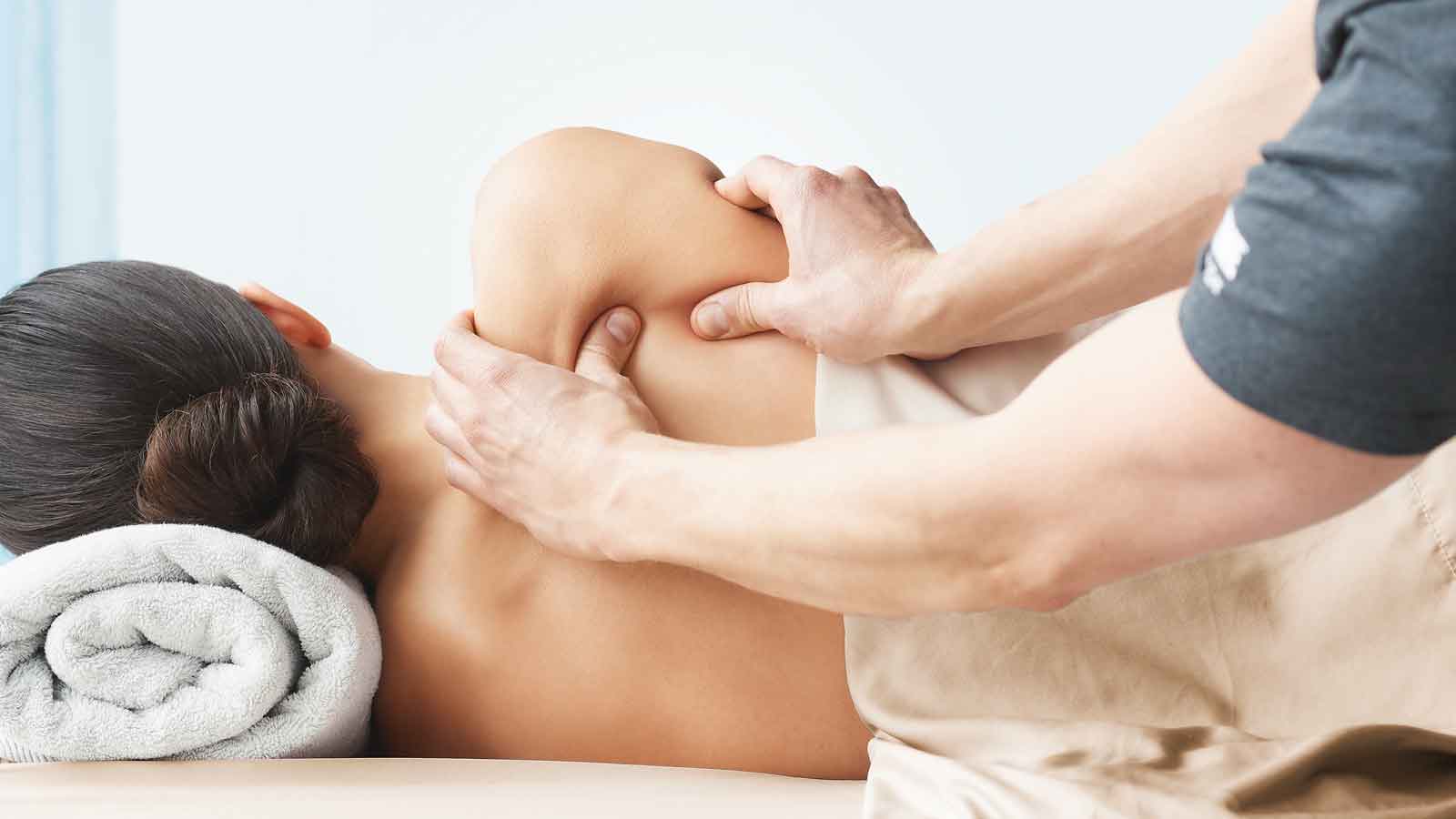A massues pressing into the shoulders of a women laying on her side on a massage table