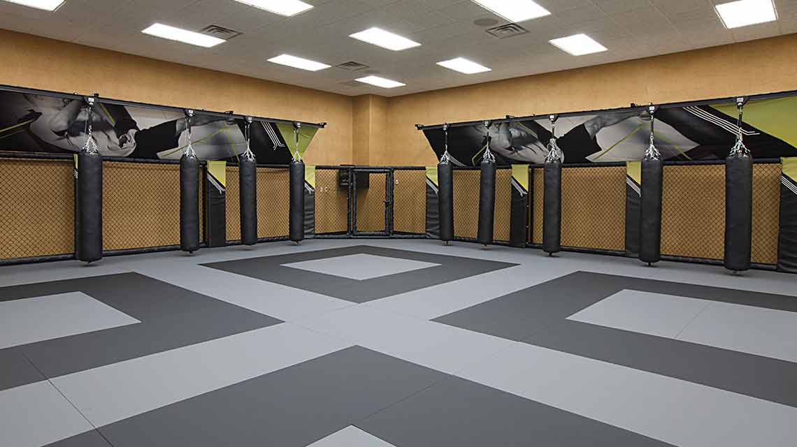 A well-lit mixed combat arts studio with a black and gray floor and walls lined with black hanging punching bags