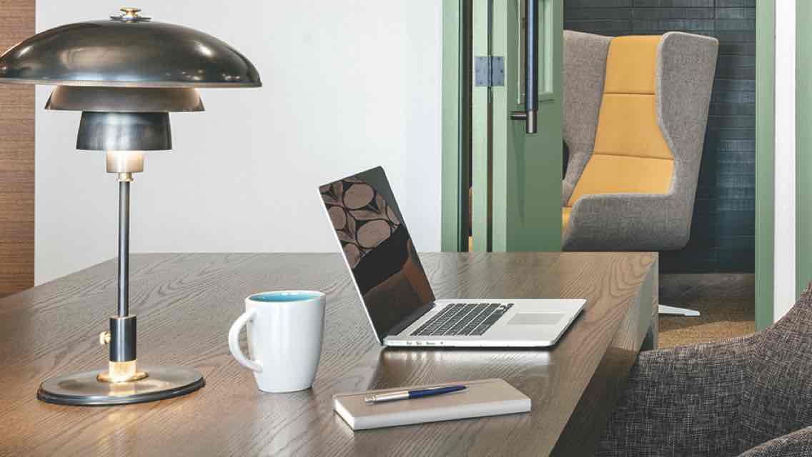 A modern workspace featuring a desk, laptop, desk lamp, coffee mug and cushioned swivel chair