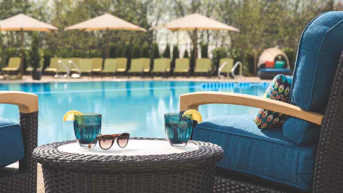 Two lounge chairs and a table with two drink glasses and a pair of sunglasses beside an outdoor leisure pool