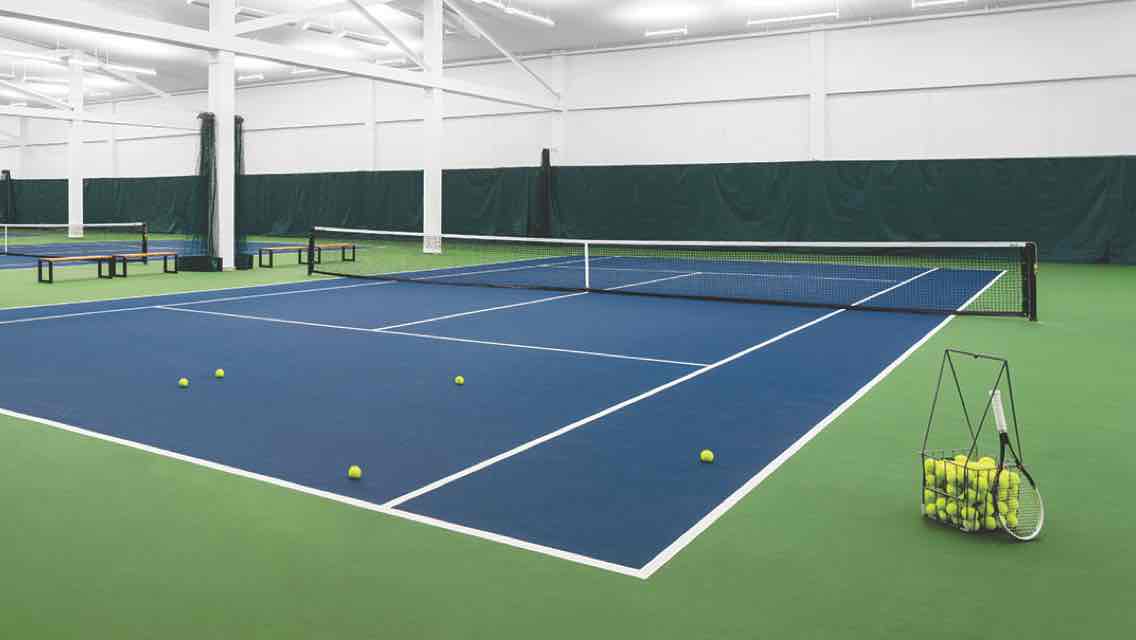 A row of indoor tennis courts with a racquet and basket of tennis balls standing by