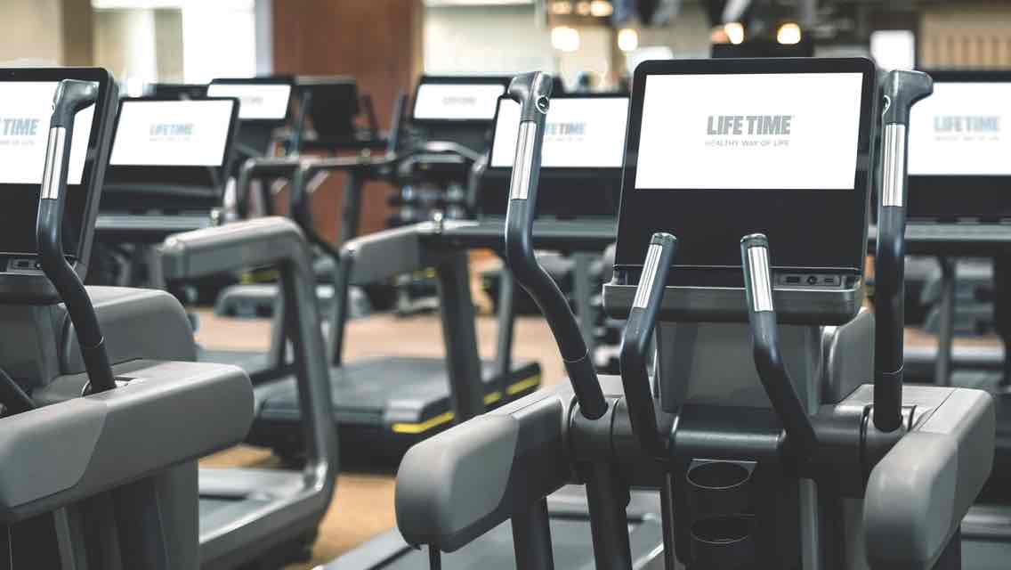 A row of state-of-the art cardio machines on a gleaming wood fitness floor