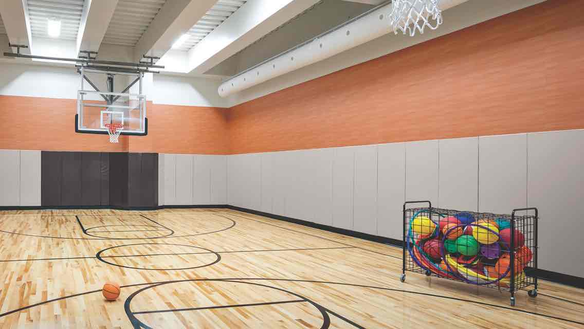 A spacious gym with a gleaming wood floor, basketball hoops and a cart filled with basketballs