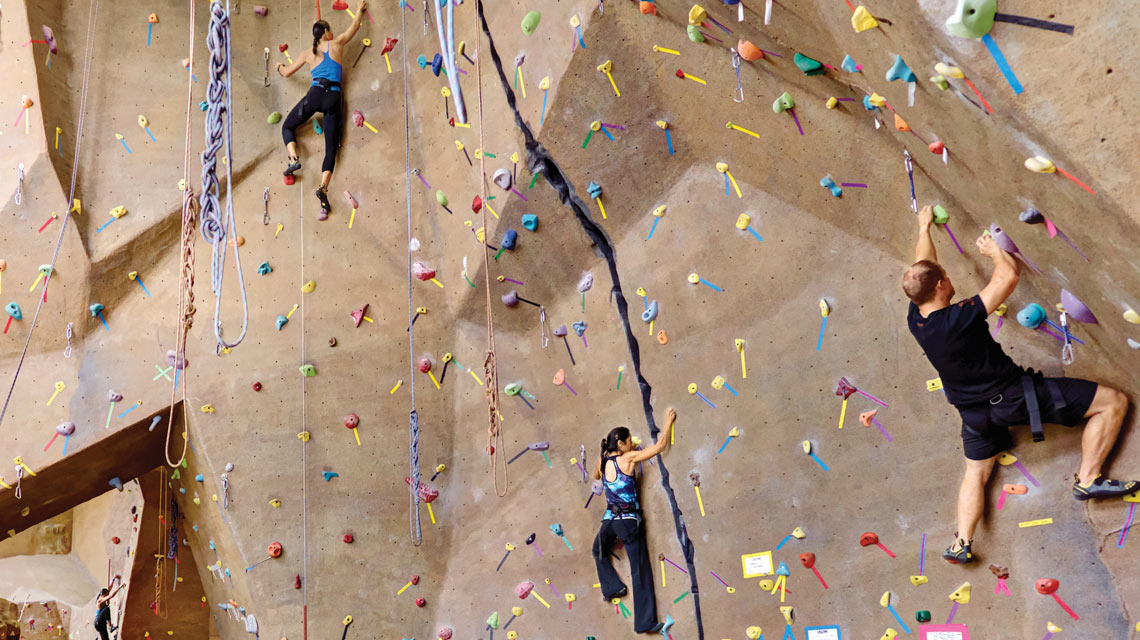 Four climbers half way up an indoor climb wall with colorful markings