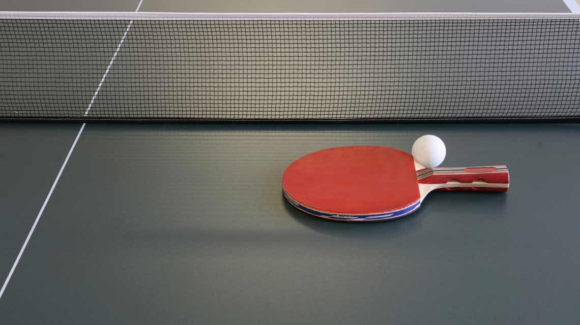 A table tennis paddle and ping pong ball sit atop a table tennis table