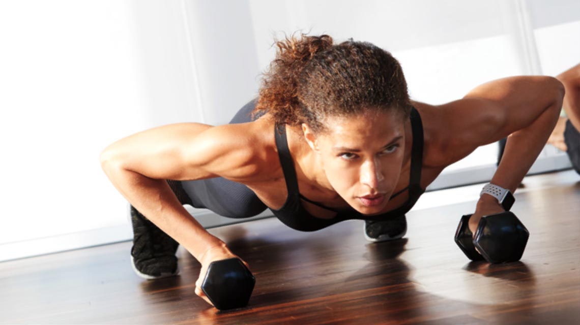 A woman holding dumbbells in a plank position for a studio class