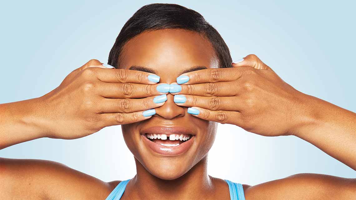 A woman covering her eyes with both hands to showcase her bright blue nail color