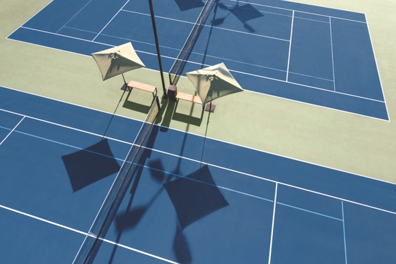 Two outdoor tennis courts separated by two umpire seats covered by sun umbrellas.