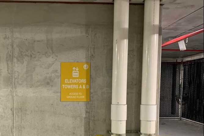 A yellow sign on an interior wall of a parking garage labeled “Elevators: Towers A & B”